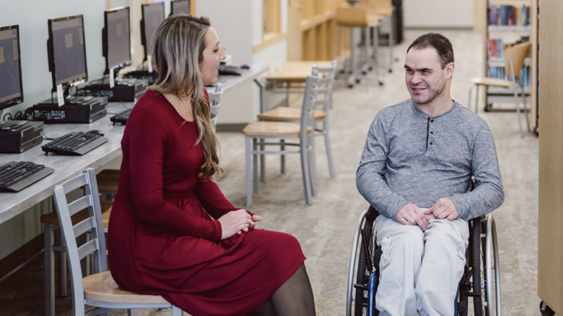 A man in a wheelchair speaks with a woman sitting in a chair.